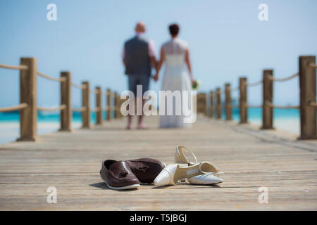 Coppia sposata sul giorno di nozze camminando romanticamente esterno sul molo in legno con un paio di scarpe in primo piano Foto Stock