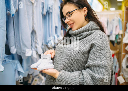 Un futuro felice madre acquista i bambini vestiti in negozio per neonati. Donna incinta in un negozio di prodotti per neonati Foto Stock