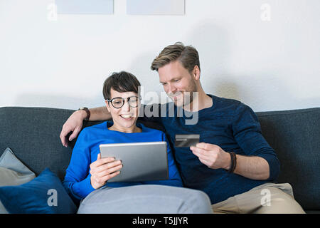 Felice casual giovane rilassante sul lettino usando tablet e azienda carta di credito Foto Stock