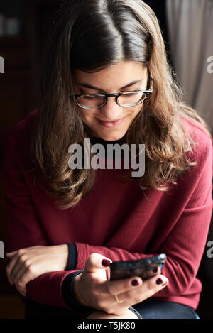 Sorridente giovane donna guardando al telefono cellulare Foto Stock