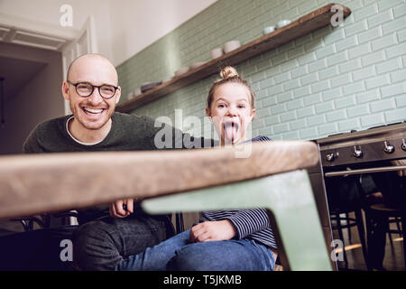 Padre e figlia seduta in cucina, ragazza tirando funny faces Foto Stock