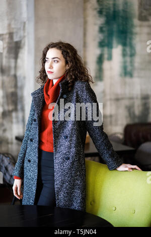 Una giovane ragazza attraente sorge in un cafe, vestito con una giacca calda. Foto Stock