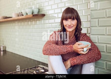 Felice donna seduta in cucina, bere il tè Foto Stock