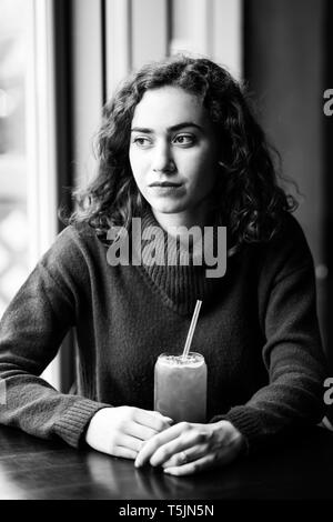 Giovane ragazza attraente si siede in un bar e beve succo di frutta. Foto Stock