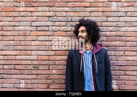 Ritratto di un giovane sorridente uomo in piedi in corrispondenza di un muro di mattoni Foto Stock