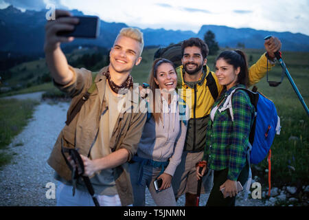 Gruppo di amici in appoggio sulla montagna mentre escursionismo. Gli escursionisti rilassante e tenendo selfie. Foto Stock