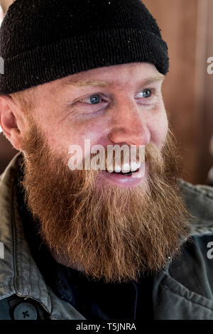 Ritratto di sorridente uomo barbuto con luce marrone capelli, vestita di nero beanie. Foto Stock