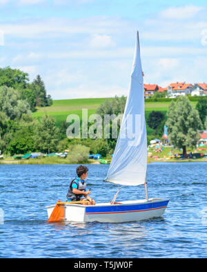 Giovane marinaio in barca a vela con il suo dinghy sul lago alpino nella regione di Allgäu Foto Stock