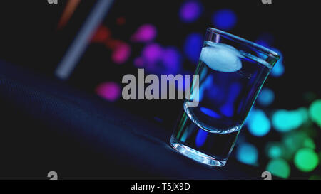 Bere shot con ghiaccio in bar su neon colore sfondo astratto Foto Stock