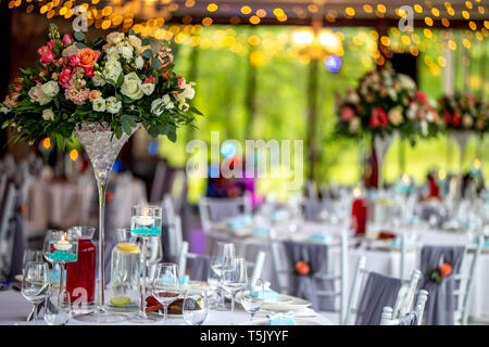 Matrimonio della decorazione della tavola. Bouquet di fiori in vaso sul tavolo accanto a piatti, bicchieri e confezioni regalo. Bouquet di fiori, bicchieri, gif Foto Stock