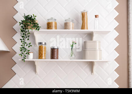 Bianco aperto ripiani di cucina, i cereali e la pasta in vasetti di vetro, spaghetti, fiori in un vaso, bottiglia di vetro, un vaso sullo sfondo della piastrella Foto Stock