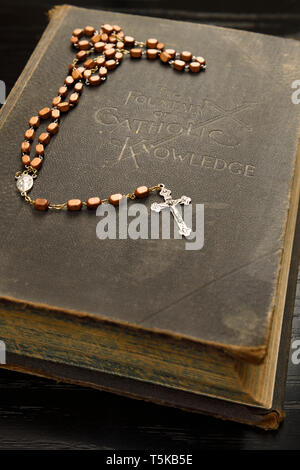 Libro antico sulla fontana della conoscenza cattolica con un santo rosario giacente sul coperchio Foto Stock