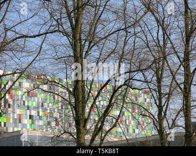 Multi-colore di rivestimento esterno in un moderno edificio universitario intravisto attraverso gli alberi in una giornata di sole da Utrecht Botanic Garden; Aprile 2019 Foto Stock