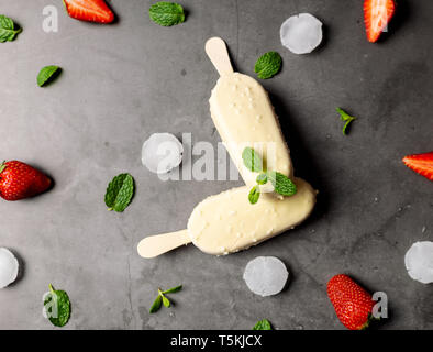 Gelato fragola stick ricoperti di cioccolato bianco, ghiaccioli , sul marmo nero tabella, laici piatta Foto Stock