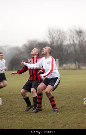 Due uomini in competizione per la testata la palla in una partita di calcio Foto Stock
