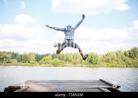 Foto dal retro del jumping uomo sul ponte di legno dal fiume al giorno Foto Stock