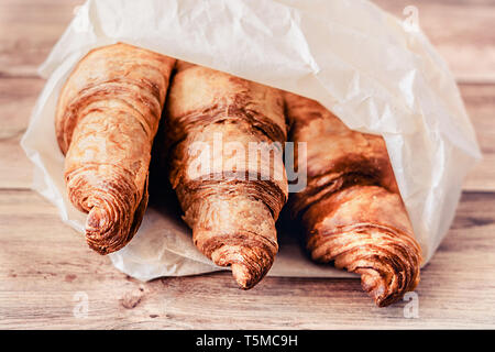 Tre dei deliziosi croissant avvolto in carta da forno su un tavolo di legno. Close-up. Foto Stock