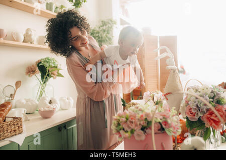 Felice madre gioca con il suo bambino in cucina su sfondo di decorazioni di pasqua. Foto Stock