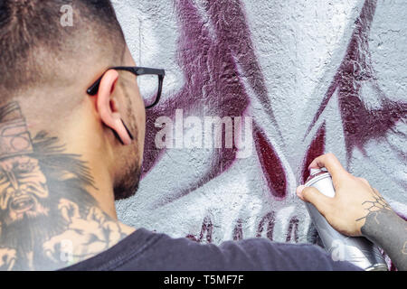 Street Graffiti artist pittura con un colore spray può un mostro scuro cranio graffiti sul muro della città outdoor - Close up vernici a mano Foto Stock