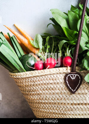 Paglia di vimini sacchetto pieno di naturali freschi ortaggi di primavera. Un sano vegetariano vegano cibo dal mercato locale dalle aziende agricole Foto Stock