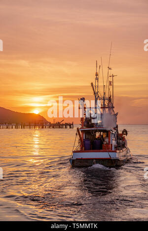 Luce bassa fisherman barca galleggiante sul mare durante il tramonto dorato Foto Stock