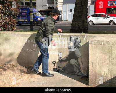 Calvin Benson, 48, mette un cappuccio di materiale in foglio di plastica su un disegno che sembra essere di artista di strada Banksy. Le opere d'arte ambientale è apparso vicino la ribellione di estinzione camp in Marble Arch, Londra. Foto Stock