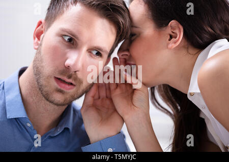 Close-up di giovane imprenditrice Whispering in Partner maschile l orecchio Foto Stock