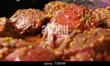 Pezzi di filetto crudo di carne di manzo marinato con semi di senape e rosmarino sono giacenti in tray nero su scaffale del negozio in slow mo close up telecamera Foto Stock