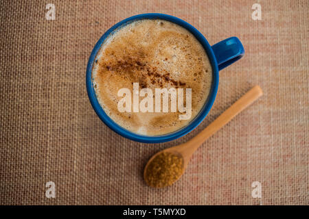 Blue tazza di caffè con latte e cannella con il cucchiaio di legno riempita con zucchero di canna Foto Stock