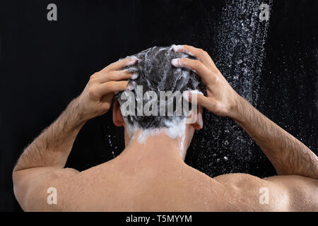 Vista posteriore dell'uomo testa di lavaggio con shampoo per doccia Foto Stock