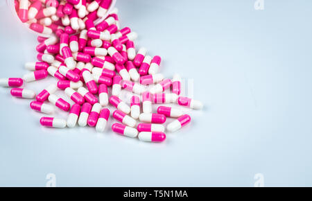 Rosa e Bianco capsule pillola versato fuori dalla bottiglia di plastica bianca contenitore. Global Healthcare concetto. Antibiotici la resistenza al farmaco. Ca antimicrobici Foto Stock