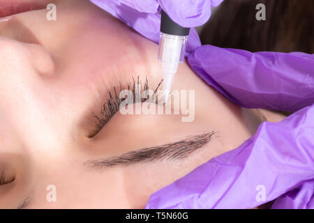 Estetista ragazza preparare per applicare eyeliner permanente tatuaggio sul giovane e bella ragazza in studio di bellezza. Tattooist rendendo eyeliner con utensile Foto Stock