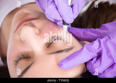 Estetista preparare per applicare eyeliner permanente tatuaggio sul giovane e bella ragazza in studio di bellezza. Tattooist rendendo eyeliner con utensile Foto Stock