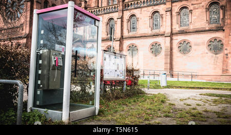 Freiburg im Breisgau, Germania - 31 dicembre 2017: Deutsche Telekom phone booth davanti a una chiesa nel centro storico della città in un giorno di inverno Foto Stock