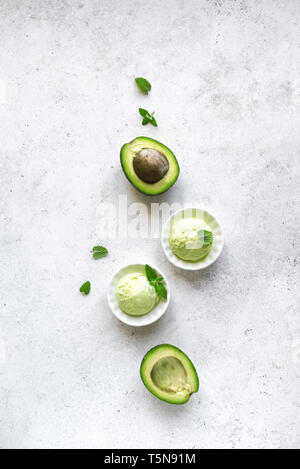 Avocado gelati su pietra bianca di sfondo, vista dall'alto, copia dello spazio. Vegano verde avocado organico o il gelato al pistacchio gelato con foglie di menta. Foto Stock