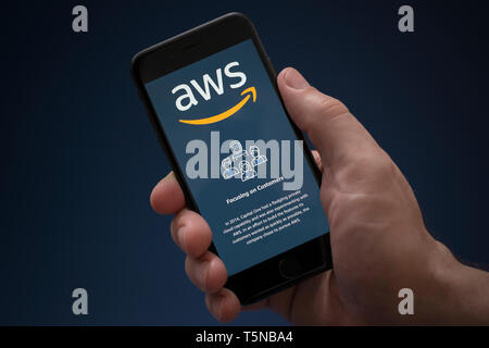 Un uomo guarda al suo iPhone che visualizza il Amazon Web Services (logo solo uso editoriale). Foto Stock