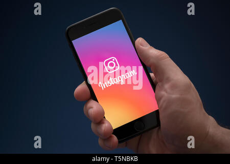 Un uomo guarda al suo iPhone che visualizza il logo Instagram (solo uso editoriale). Foto Stock