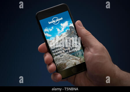 Un uomo guarda al suo iPhone che consente di visualizzare la guida della Lonely Planet logo (solo uso editoriale). Foto Stock