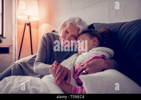 Grey-haired granny abbracciando il suo malati ragazza carina di addormentarsi Foto Stock