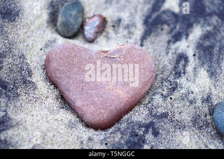 Rosso cuore di pietra, mare pietra a forma di cuore sulla sabbia Foto Stock