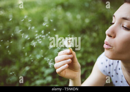 Giovane donna di soffiaggio fiore di dente di leone Foto Stock