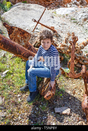 Ragazzo seduto su un enorme Rusty ancoraggio. La Grecia. Foto Stock