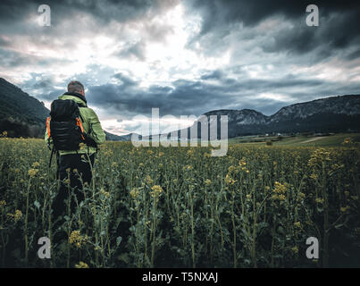 Un uomo in piedi su un campo in erba sta guardando la vista sulla montagna su un molto giorno nuvoloso al mattino. Foto Stock