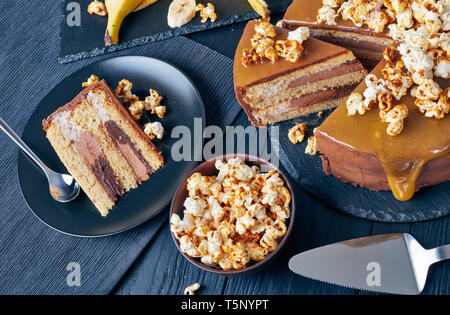 Fette di banana pan di spagna a strati con burro di arachidi mousse e guarnita con glassa al cioccolato fuso caramello e popcorn dolce, vista da sopra, ingr Foto Stock