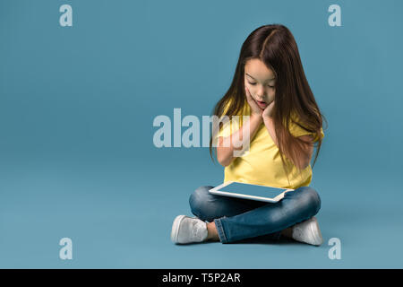 Sorpreso grazioso fanciullo ragazza con vuoto computer tablet su sfondo blu Foto Stock