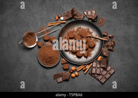 Tartufi di cioccolato caramelle, pezzetti di cioccolato e cacao in polvere su scuro dello sfondo in calcestruzzo Foto Stock