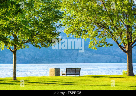 Banco a riva che si affaccia sul lago e le montagne su sunset Foto Stock