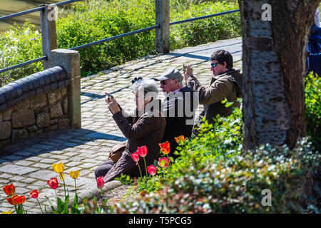 Tre turisti seduti su una panchina (vicino al fiume Severn) scattano foto di un simbolo di Ironbridge, Telford, Regno Unito. Foto Stock