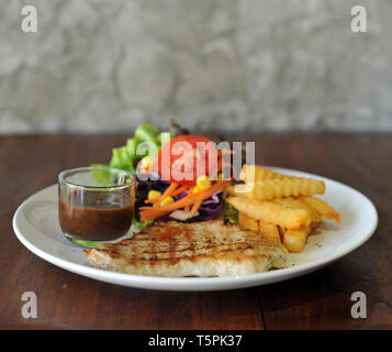 Piatto di carne di maiale alla griglia bistecca con patate fritte e insalata su uno sfondo di legno Foto Stock