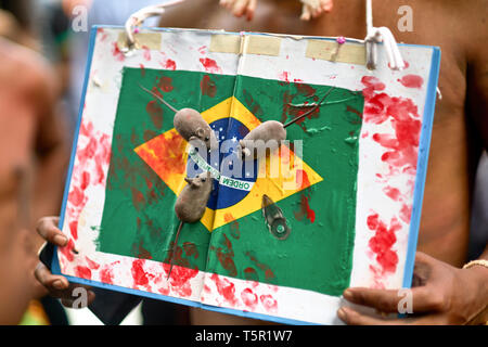 Brasilia, Brasile. 26 apr, 2019. Un uomo detiene un brasiliano bandiera di cartone con macchie rosse e ratti di mangiarlo. La protesta degli Indiani a Brasilia per la protezione del loro habitat. Presidente Bolsonaro vuole ridurre la protezione della regione amazzonica e utilizzare la foresta pluviale più economicamente. Credito: Pablo Albarenga/dpa/Alamy Live News Foto Stock